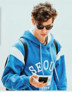 a young man in a blue hoodie looking at his cell phone while wearing sunglasses