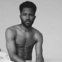 a shirtless man sitting on top of a bed next to a white sheet covered wall