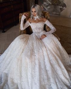 a woman sitting in a chair wearing a wedding dress with long sleeves and an open back