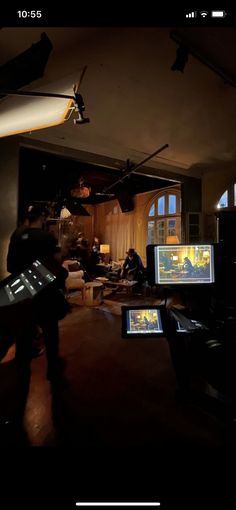 two people are sitting in a dark room with three monitors on the desk and one person is holding a video game controller