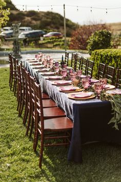 a long table is set with plates and place settings for an outdoor dinner party in the grass