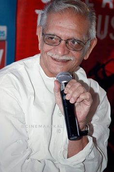 a man holding a microphone in his right hand while wearing glasses and a white shirt