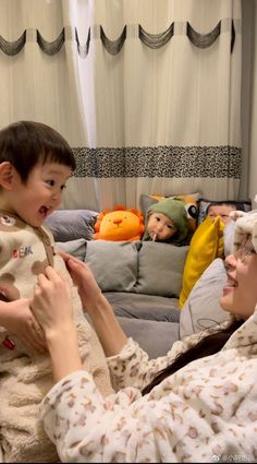 a woman holding a child in her arms while they look at stuffed animals on the couch