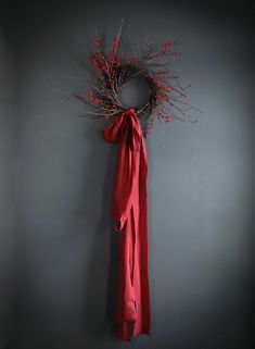 a red ribbon hangs on the wall next to a twig wreath with berries hanging from it