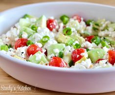 a white bowl filled with cucumber, tomatoes and feta on top of a wooden table