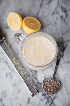 two lemons are sitting next to a cup of liquid on a marble counter top