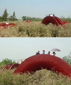 three people sitting on top of a red structure in the middle of a grassy field