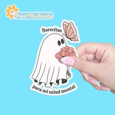 a hand holding up a sticker with a ghost on it's face and flowers in its mouth