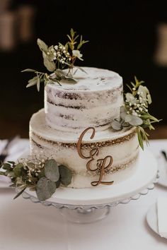 a three tiered wedding cake with greenery and initials on the top is sitting on a table