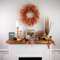 a mantel with a wreath, candles and pictures on it