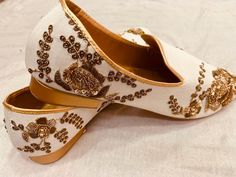 two pairs of white shoes with gold embellishments