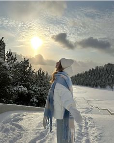 a woman standing in the snow wearing a white hat and scarf with her arms outstretched