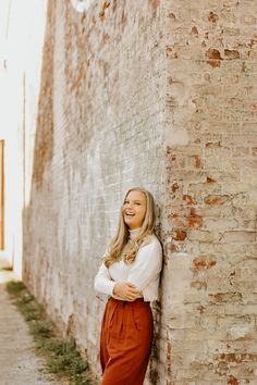 a smiling woman leaning against a brick wall