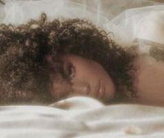 a woman laying on top of a bed with her head resting on the pillow next to her