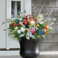 a black vase filled with christmas ornaments and greenery