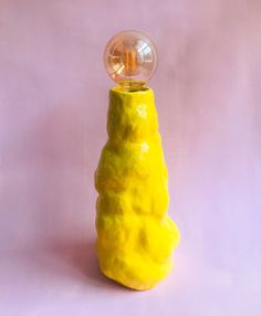 a small yellow object with a light on it's top sitting in front of a pink background