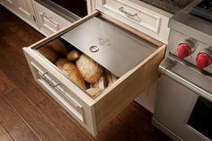 an open drawer in the middle of a kitchen with some breads inside and on it