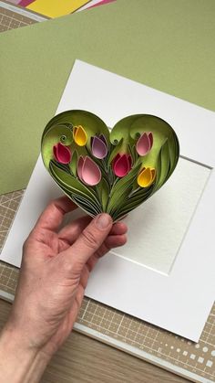 a hand holding a paper heart with flowers on it