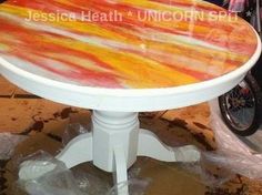 a white table with orange and yellow paint on it sitting in front of a motorcycle