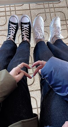 two people sitting on the ground making a heart with their hands