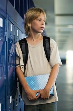 a young woman standing in front of lockers holding a blue folder and looking off into the distance