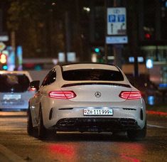 the back end of a white car driving down a street at night with traffic lights in the background