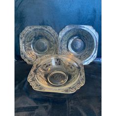 three glass dishes sitting on top of a black cloth covered table next to each other