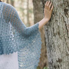 a woman standing next to a tree wearing a shawl and holding onto the trunk