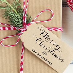 a christmas present wrapped in brown paper with red and white twine on it next to a sprig of pine