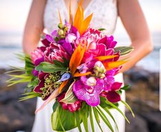 a woman holding a bouquet of flowers near the ocean