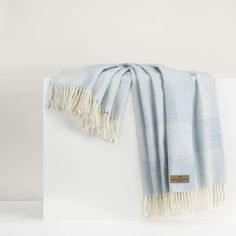 the light blue and white scarf is folded on top of a white block with fringes