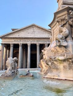 the fountain in front of the building has statues on it's sides and is surrounded by columns