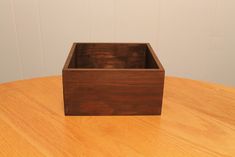 a square wooden box sitting on top of a wooden table next to a white wall