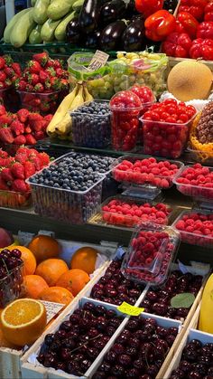 an assortment of fruits and vegetables on display at a market stall, including cherries, oranges, strawberries, bananas