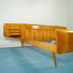 a wooden bed frame sitting on top of a blue floor next to a white wall