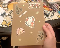 someone holding up a brown notebook with stickers on it