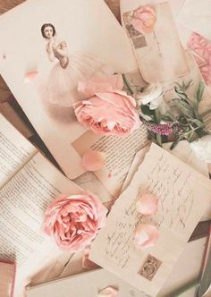 an open book with pink flowers on top of it next to some old letters and envelopes