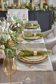 the table is set with gold and white plates, silverware, and greenery