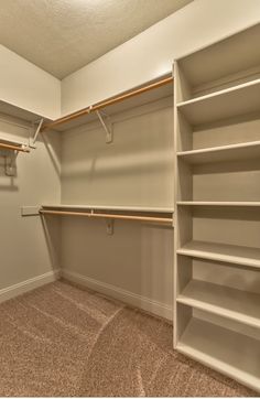 an empty walk in closet with white shelving and tan carpeting on the floor