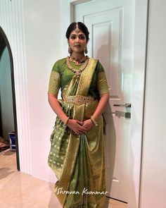 a woman standing in front of a door wearing a green and gold sari