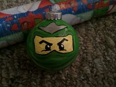 a green ornament with a face painted on it sitting next to a roll of wrapping paper