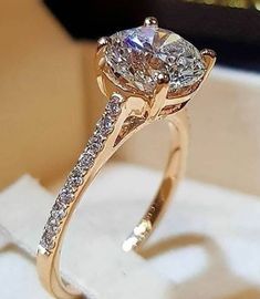 a close up of a diamond ring on a white cloth with a box in the background