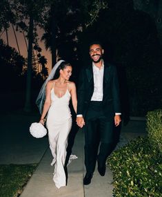 a bride and groom walking down the sidewalk at night with palm trees in the background