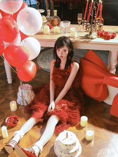 a woman sitting on the floor in front of a table with red balloons and candles