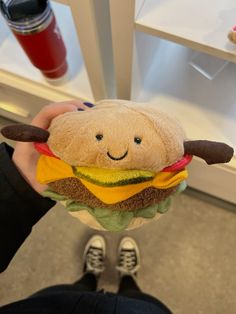 a person holding a stuffed hamburger with a smile on it's face in front of a refrigerator