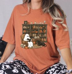 Ghost Reading Book T-shirt, Halloween Bookshelf Shirt, Cute Ghost Shirt, Funny Halloween, Black Cat Tee, Halloween Party, Halloween Gift Welcome to MadelinebyOMR  HOW TO ORDER  ➤ Browse through all the listing photos carefully. ➤ Select your desired size and color from the drop-down menus. ➤ Choose the quantity you want. ➤ Click the "Add to Cart" button. ➤ Fill in the personalization box if applicable. ➤ You can either continue shopping or proceed to checkout. ➤ Click "Proceed to Checkout" to fi Bookish Halloween Graphic Print Top, Bookish Graphic Print Top For Halloween, Halloween Bookshelf, Ghost Reading Book, Ghost Reading, Halloween Black Cat, Book Tshirts, Ghost Shirt, Cat Tee