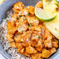 a bowl filled with rice, chicken and pineapples next to a slice of lime