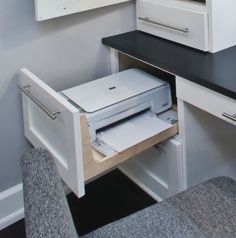 an open drawer in the corner of a desk with a printer and mouse on it