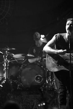 a man holding a guitar in front of a microphone and drums on stage at a concert