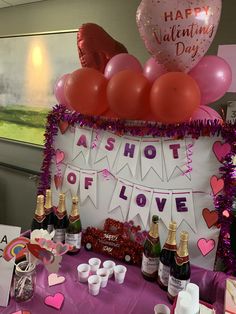 a table topped with lots of bottles of champagne and heart shaped balloons in front of a sign that says happy valentine's day